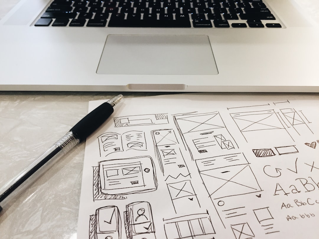 Business owner reviewing a slow, outdated website on a laptop while comparing mobile and desktop layouts with redesign notes on a desk